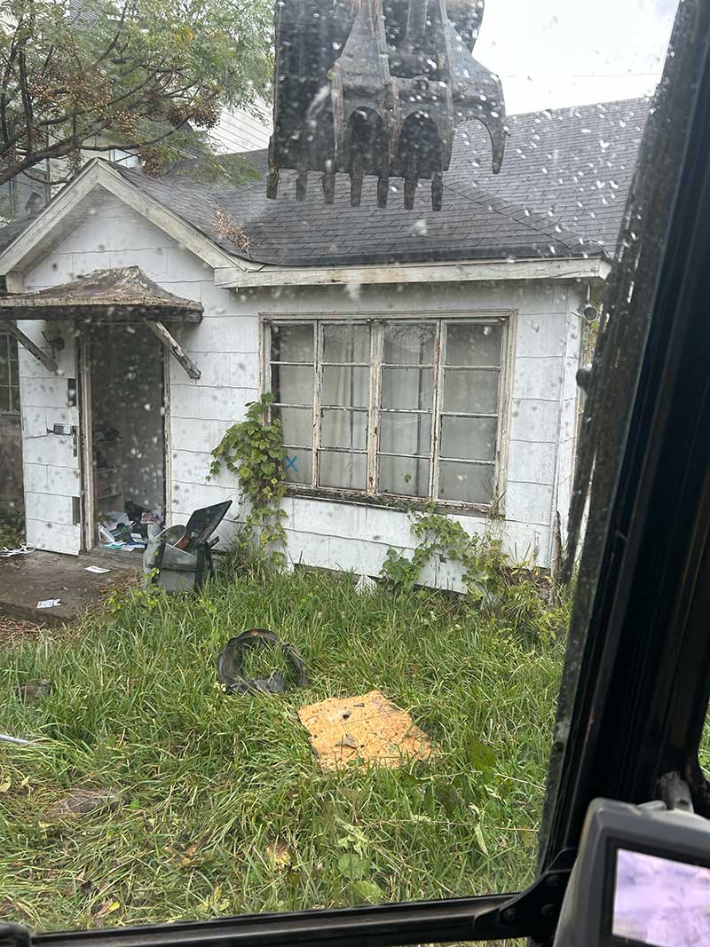 Abandoned house with overgrown grass and debris.