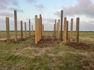 Wooden poles in open field under cloudy sky.